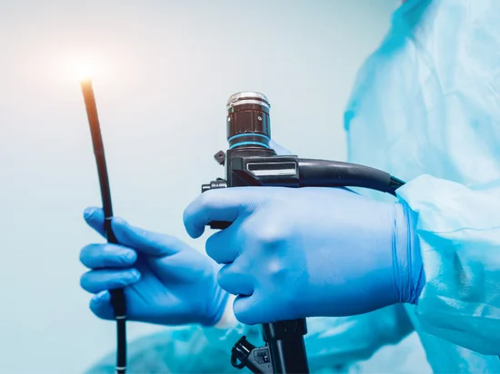 A specialist in blue surgical gloves holding an endoscope, a flexible tube with a light and camera used for colonoscopy and endoscopy.