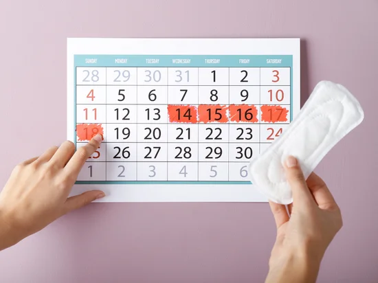 A wall calendar with specific dates marked in red, accompanied by a hand holding a menstrual pad, highlighting menstrual tracking and irregular period management techniques.