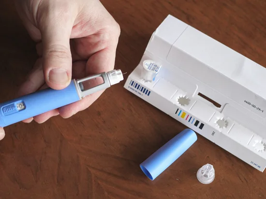 Hand holding Liraglutide injection pen on table for weight management treatment.