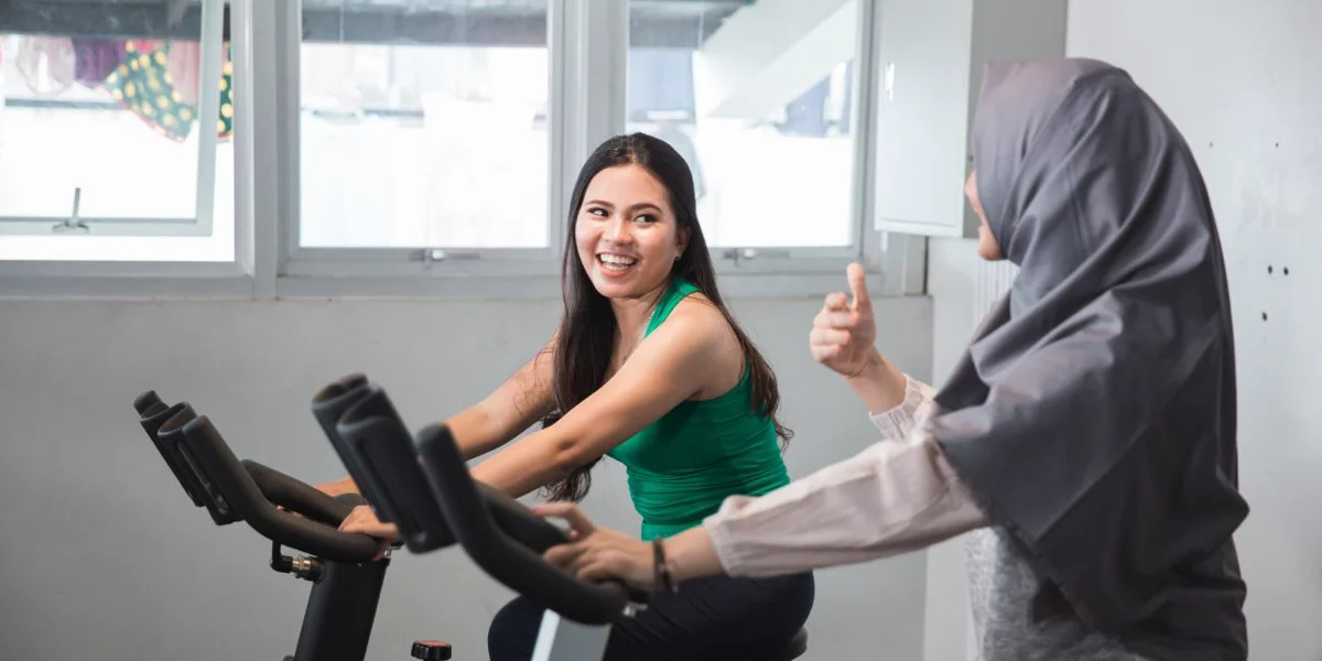 Two women exercising on stationary bikes emphasising the importance of physical activity to reduce the risk of alzheimer's disease.