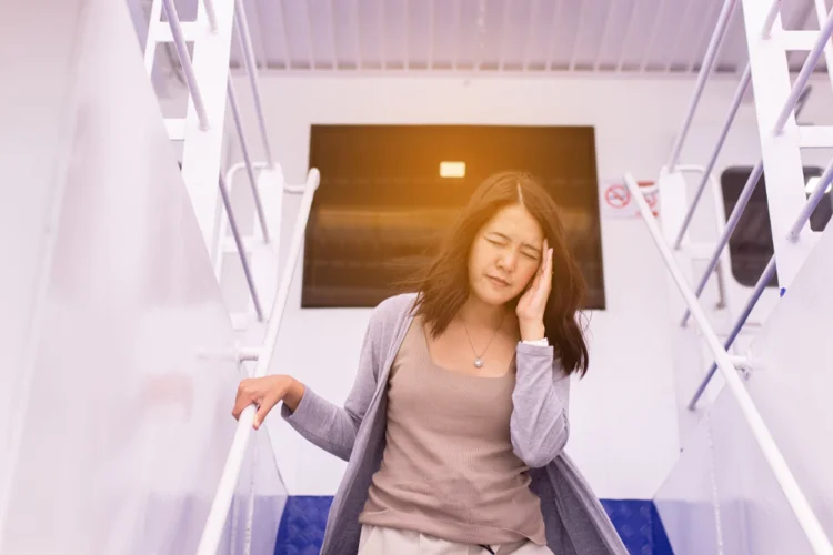 Asian woman holding her head on a boat, showing signs of motion sickness under sunlight.