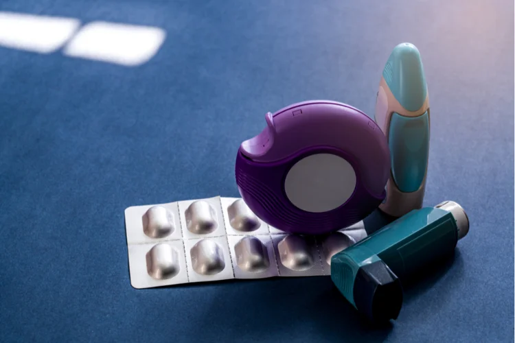 Assortment of asthma inhalers and medication arranged on a blue background, essential tools for treating and managing respiratory conditions.