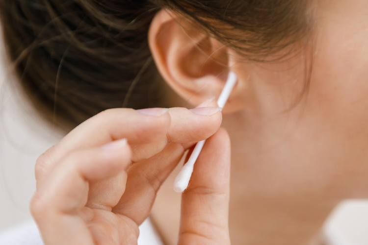 Close-up of a woman using a cotton bud in the ear, a common lifestyle cause of ear wax impaction.