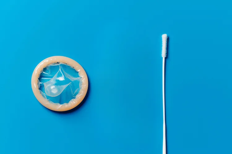 Condom and swab on blue background representing Mycoplasma genitalium prevention and screening.