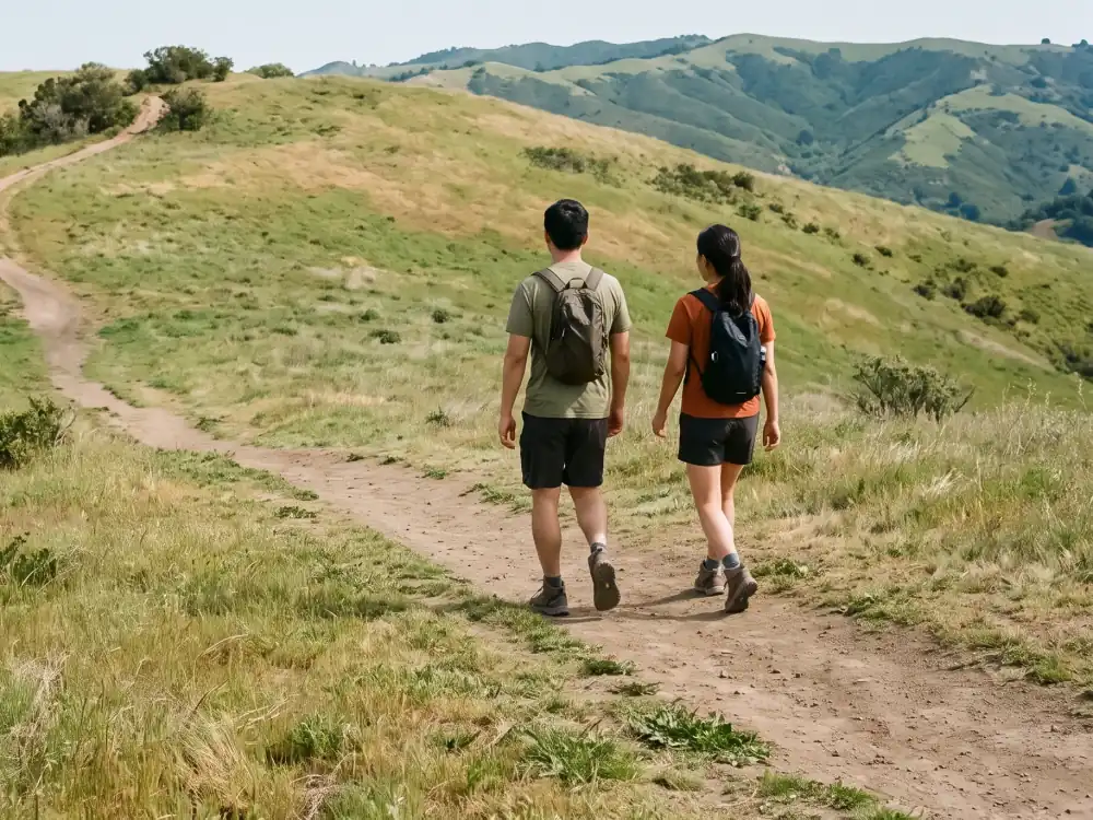 Couple with backpacks hiking along a grassy hillside trail