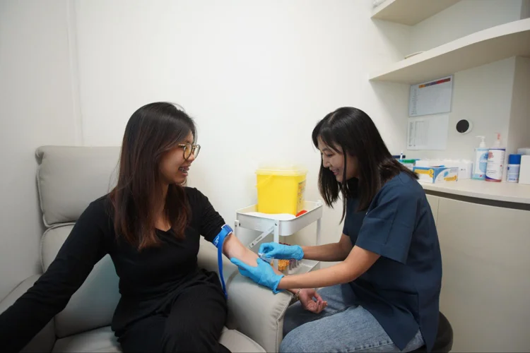 Doctor drawing blood from a woman to conduct blood investigations as part of basic health screening in singapore.