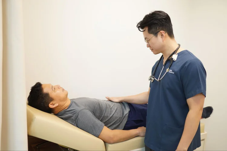 Doctor examining a mans abdomen as part of basic health screening in singapore.