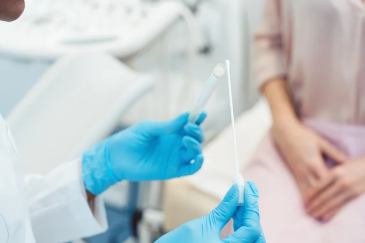 Doctor holding swab and specimen tube to collect sample for candidiasis diagnosis in female patient.