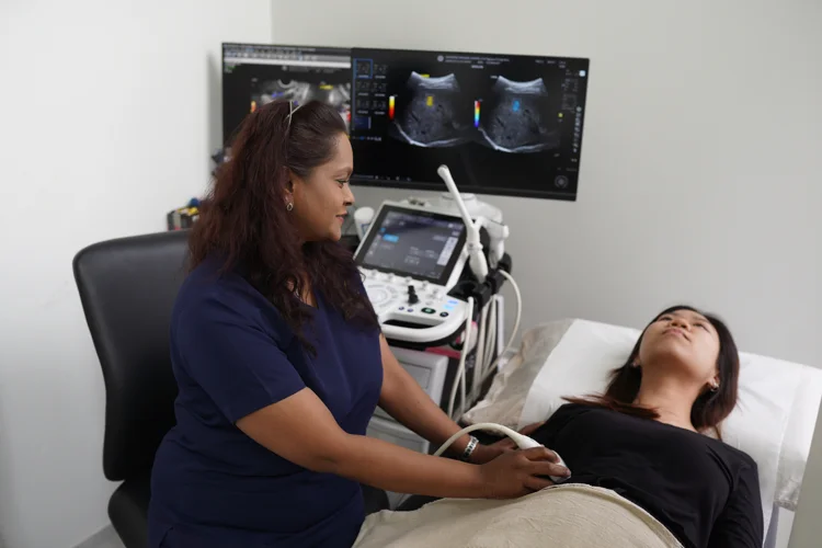 Imaging technician performing ultrasound-based elastography on a young female patient by measuring the speed of sound waves to evaluate tissue stiffness.