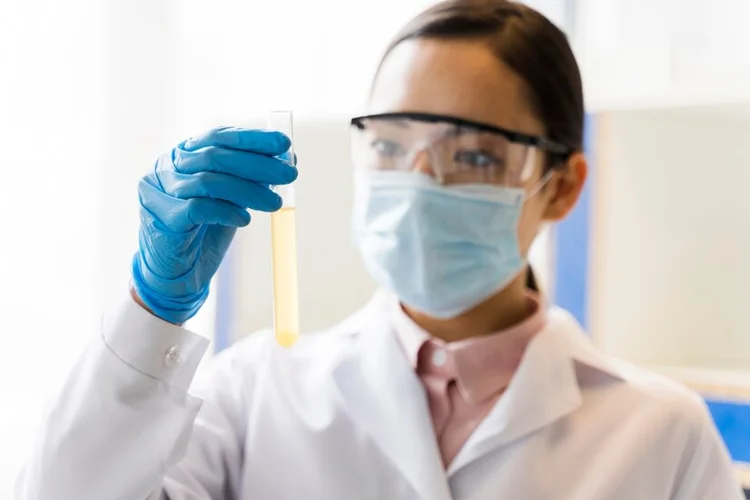 Laboratory technician holding test tube for urine analysis.