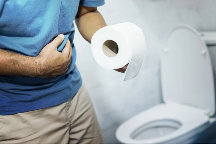 Man holding his stomach and toilet paper, suffering from diarrhoea while standing in the bathroom.