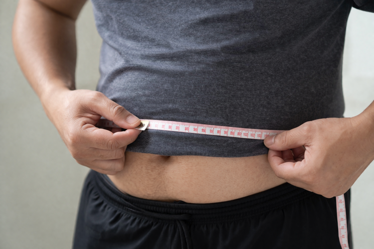 Man measuring his waist with a tape measure as part of weight management.