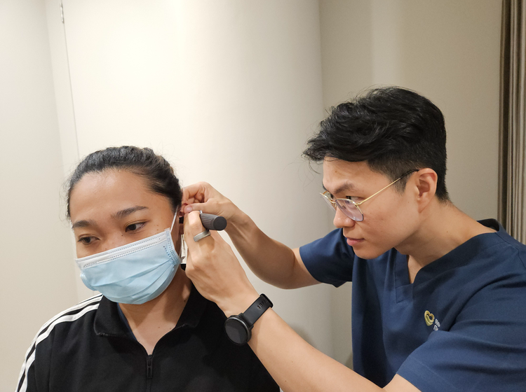 Doctor at ATA Medical examining a patient's ear canal with an otoscope before ear wax removal.