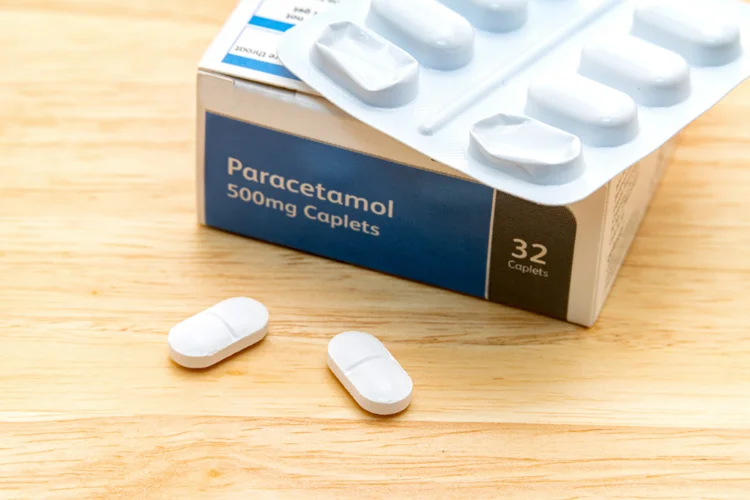 Paracetamol 500 mg caplets on a wooden table, used to reduce fever and relieve body aches caused by the flu.