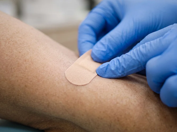 Gloved hands pressing a small plaster onto the inside of a patient's forearm.