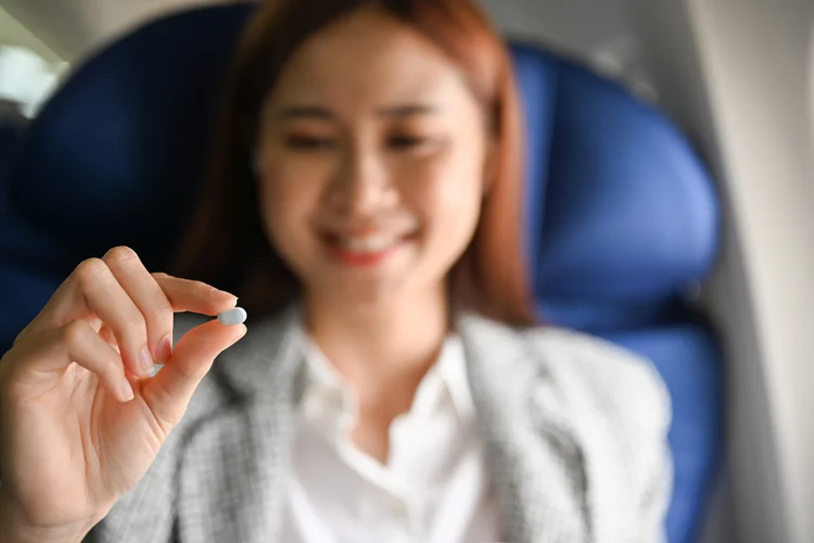 Smiling woman on an airplane holding a motion sickness pill before travel.