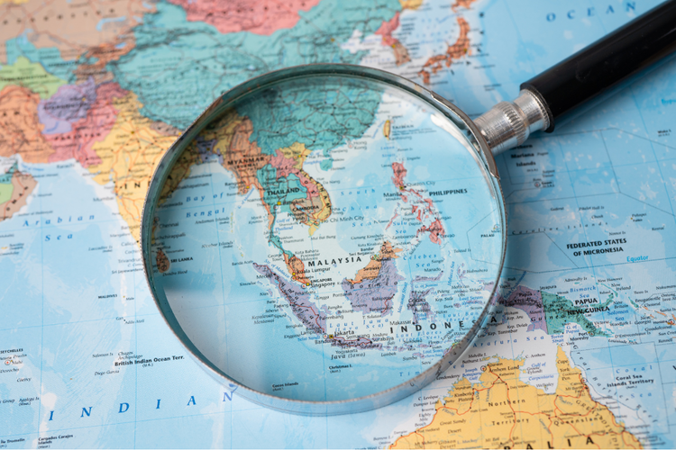 Magnifying glass highlighting South East Asia on world map for travel planning.