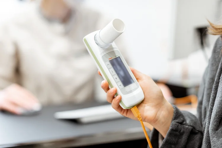 Person using spirometer during lung function test under clinical supervision.