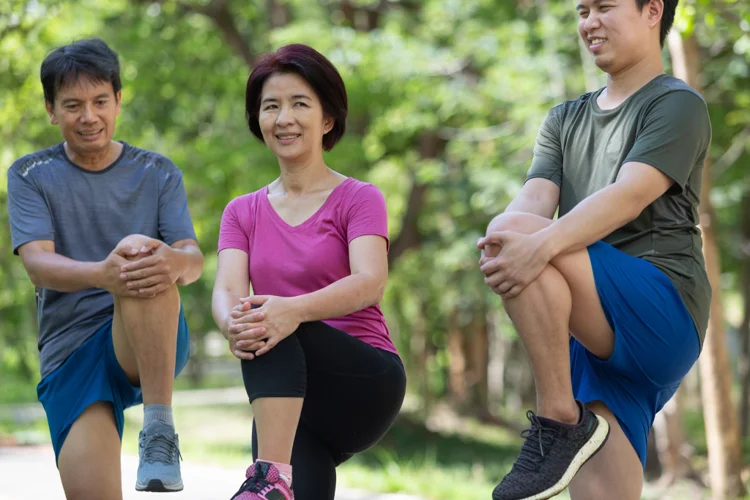 Three Singaporeans stretching in a green park, promoting healthy lifestyle changes for better diabetes management.