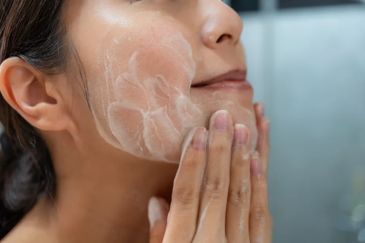 Woman cleansing face with foaming wash as part of daily skincare to prevent acne breakouts.