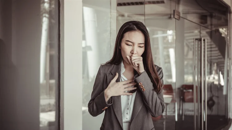 Woman experiencing severe coughing with her hand on her chest, representing symptoms of whooping cough, a contagious respiratory disease in Singapore.