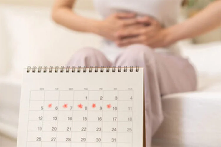 Woman holding lower abdomen with menstrual calendar in foreground to track period on birth control.