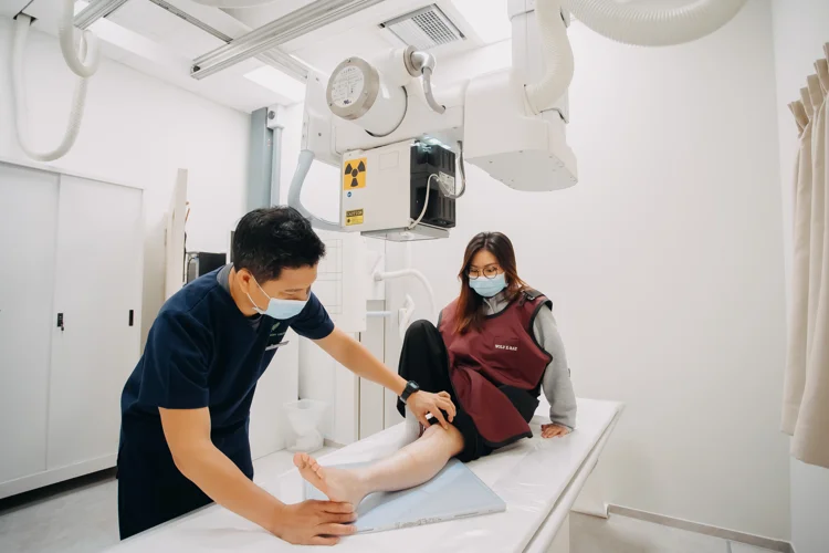 Female patient getting ready to undergo X-Ray procedure with a male staff assisting with the preparations.