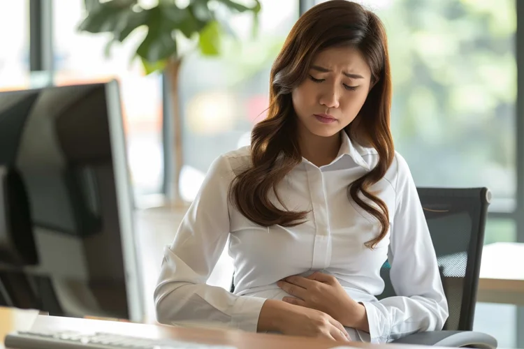 Young Asian woman experiencing stomach discomfort as a side effect of taking a period delay pill to postpone menstruation.