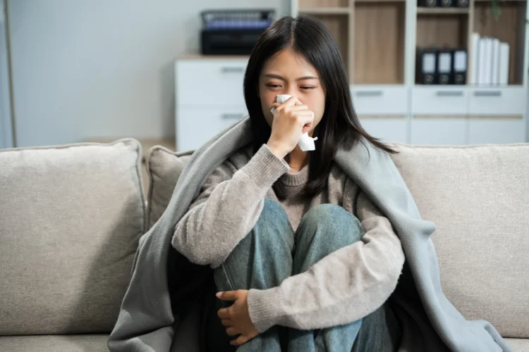 Young Singaporean woman with mild flu symptoms sitting on sofa, indicating signs of CMV infection.